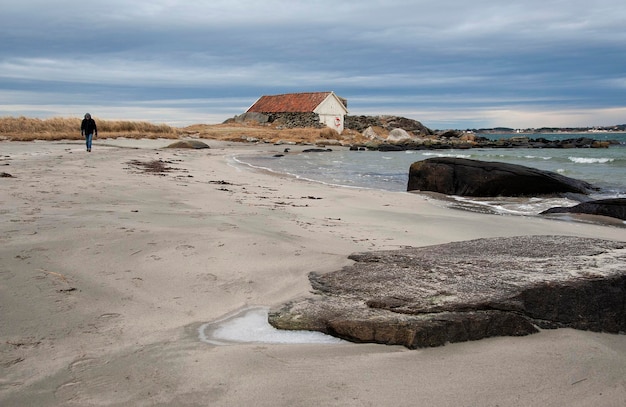 Volledige lengte van een man die op het zand loopt op het strand tegen bewolkte lucht