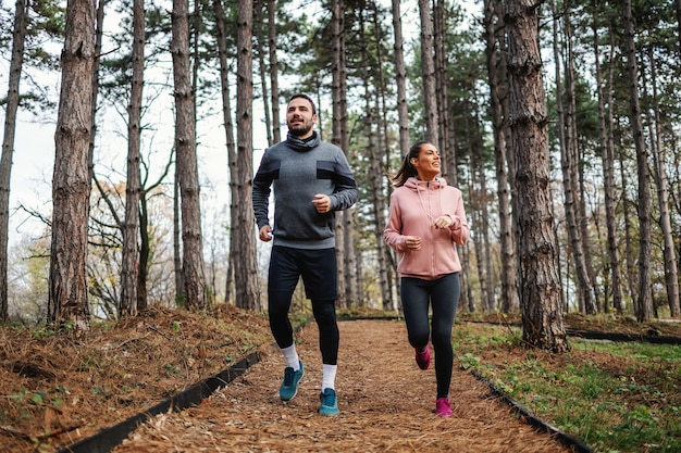 Volledige lengte van fit paar loopt door bos in de herfst en voorbereiden op marathon