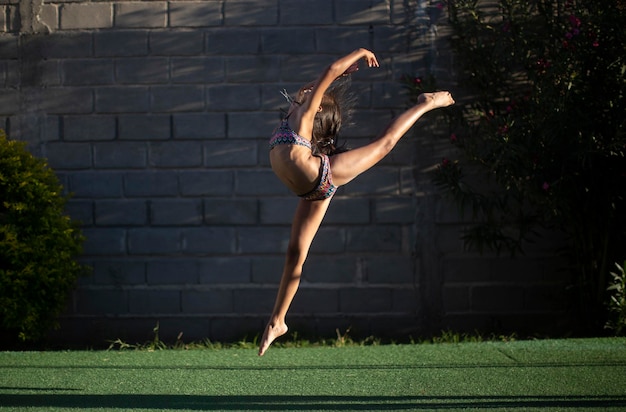 Volledige lengte van flexibele vrouw die een bikini draagt terwijl ze tegen de muur danst
