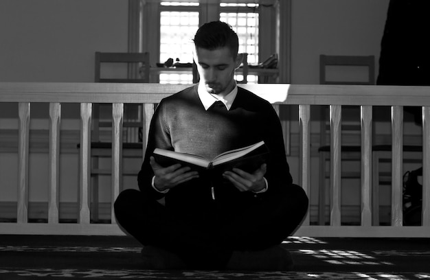 Volledige lengte van geconcentreerde jonge man die een boek leest terwijl hij tegen de reling zit
