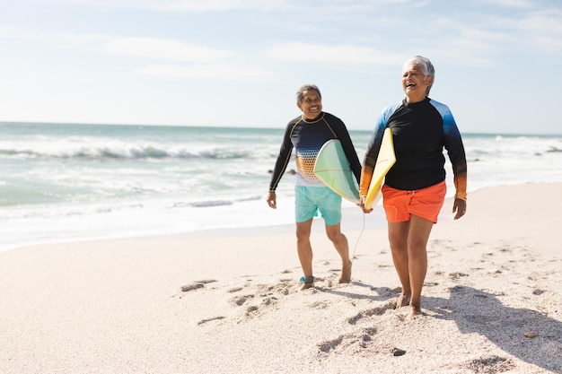 Volledige lengte van gelukkig multiraciaal senior koppel dat met surfplanken loopt op zand op zonnig strand