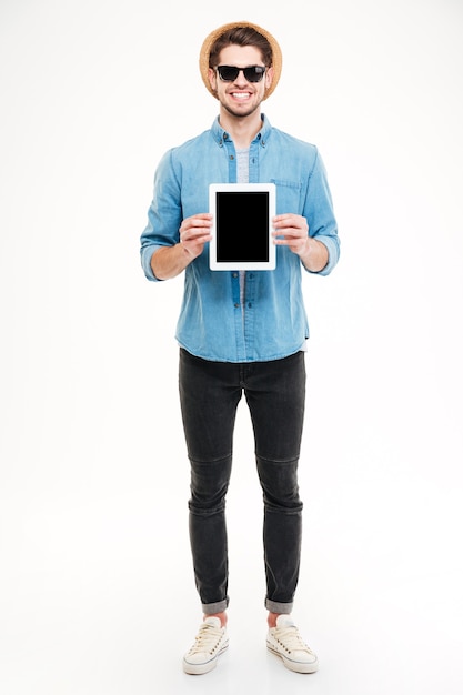 Volledige lengte van glimlachende knappe jonge man die staat en een tablet met een leeg scherm vasthoudt