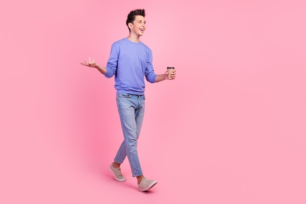Volledige lengte van jonge blanke gelukkig lachende man houdt papieren kopje warme koffiedrank geïsoleerd op pastelkleurige achtergrond