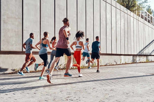 Foto volledige lengte van jonge mensen in sportkleding die joggen tijdens het sporten op het trottoir buitenshuis