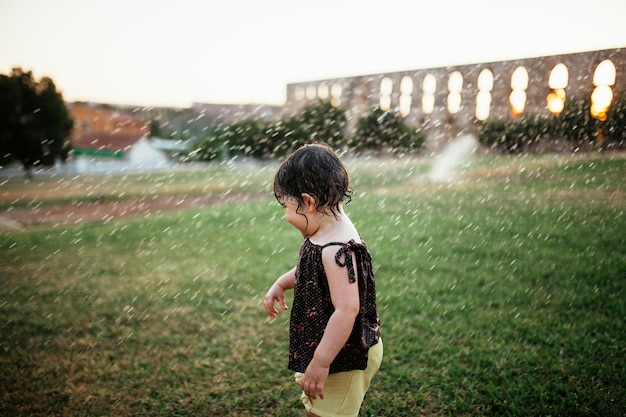 Volledige lengte van kind dat met watersprinkelaars speelt
