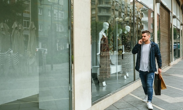 Volledige lengte van knappe jonge man die aan het praten is op een smartphone terwijl hij door de winkel loopt