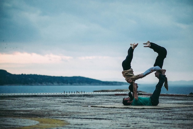 Foto volledige lengte van man die vrouwen op voeten balanceert bij de zee tegen bewolkte lucht