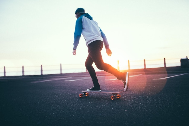 Volledige lengte van man skateboarden op de weg tegen de lucht