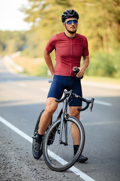 Volledige lengte van mannelijke atleet rusten op verharde weg met fiets en fles met water te houden