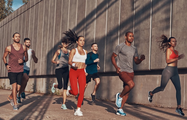 Volledige lengte van mensen in sportkleding die joggen terwijl ze buiten op het trottoir trainen