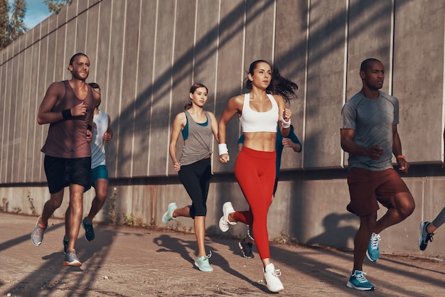 Volledige lengte van mensen in sportkleding die joggen terwijl ze buiten op het trottoir trainen