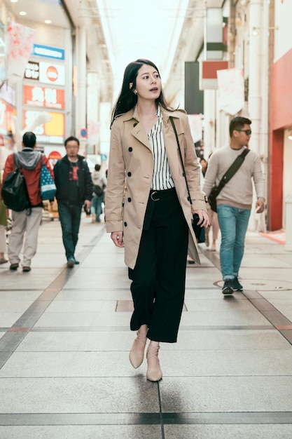 Volledige lengte van mooie jonge vrouw op zakenreis naar osaka japan winkelen in shinsaibashi. kantoordame op zoek naar een souvenircadeau om te kopen in de moderne stad. elegante vrouw op hoge hakken