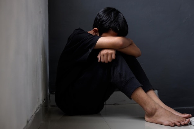 Volledige lengte van ongelukkig kind met een geestelijke gezondheidsprobleem zit op de vloer en bedekt het hoofd met handen