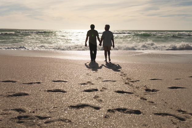 Volledige lengte van senior multiraciaal koppel hand in hand wandelen op het strand met voetafdrukken op zonnige dag