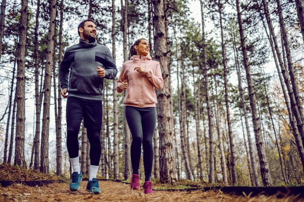 Volledige lengte van vrolijk jong koppel in sportkleding die in de natuur loopt.