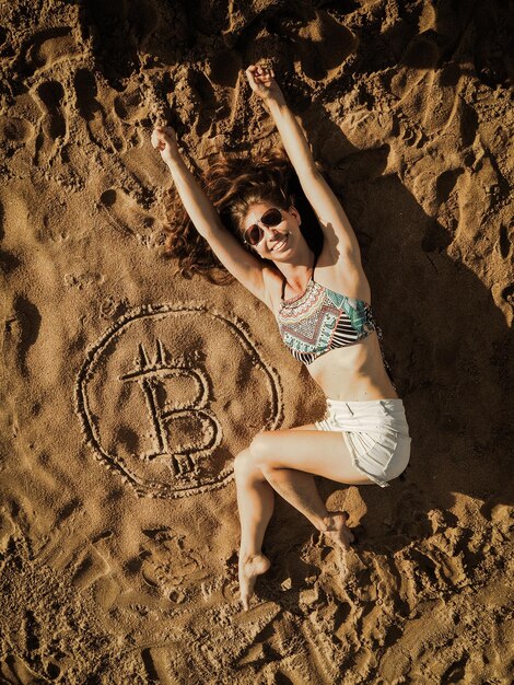 Foto volledige lengte van vrouw die ligt bij bitcoin symbool op het strand