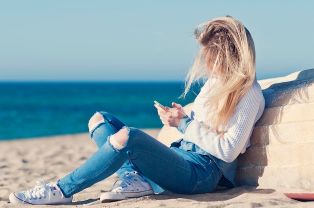 Volledige lengte van vrouw die mobiele telefoon gebruikt terwijl ze op het strand rust