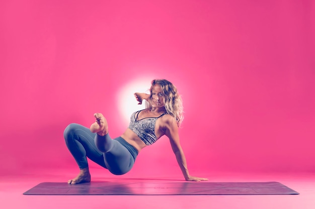 Foto volledige lengte van vrouw die oefent tegen een roze achtergrond