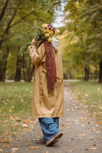 Volledige lengte van vrouw verbergend gezicht met bos gele bloemen in park in herfstseizoen