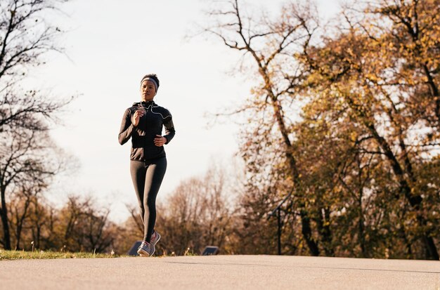 Volledige lengte van zwarte sportvrouw joggen tijdens herfstdag in de natuur kopieer de ruimte