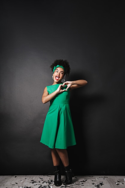 Volledige lengtefoto van jonge afro Amerikaanse dame die groene kleding draagt die hartvorm met vingers toont