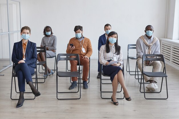 Volledige multi-etnische groep zakenmensen die maskers en sociale afstand dragen terwijl ze op stoelen in het publiek zitten tijdens een zakelijke conferentie of seminar