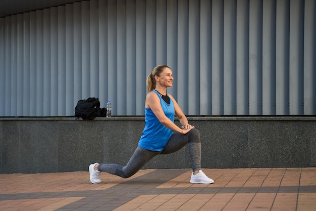 Volledige opname van een mooie sportieve volwassen vrouw in sportkleding die glimlacht tijdens het opwarmen