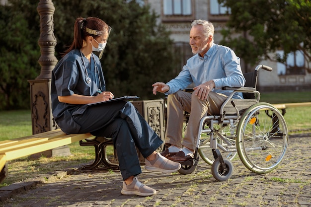 Volledige opname van herstellende mannelijke patiënt in rolstoel die zijn gezondheidstoestand bespreekt met
