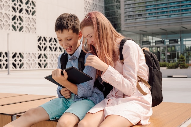 Volledige opname van twee jonge tienerbroers en zussen die digitale tablet gebruiken in de buurt van school en huiswerk maken, concept van het gebruik van technologie in modern onderwijs modern