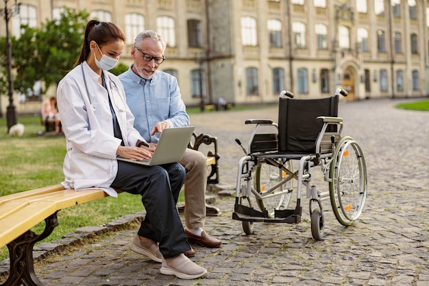 Volledige opname van volwassen herstellende patiënt met rolstoel zittend op de bank in het park in de buurt