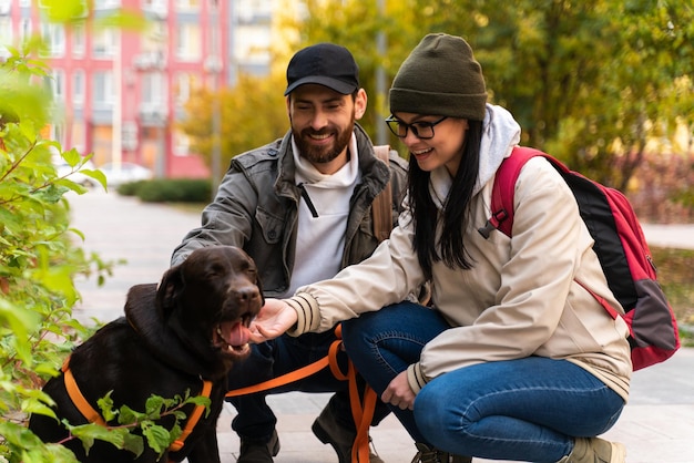 Volledige weergave van het verliefde blanke paar geknield bij hun mooie bruine Labrador-hond en zich gelukkig voelend tijdens het herfstwandelen