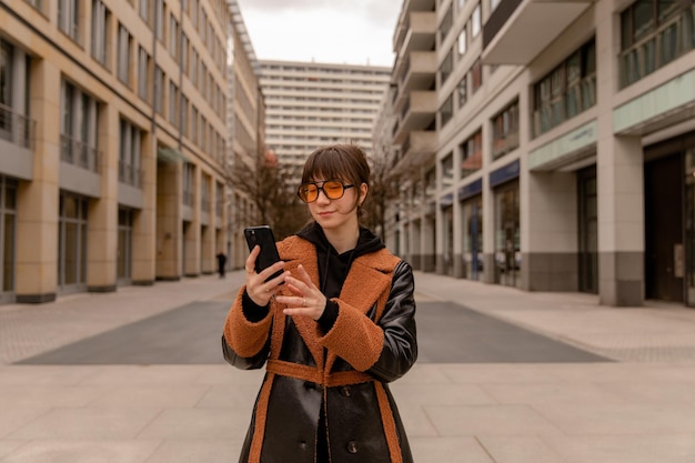 Volledige weergave van vrouw op straat glimlach op telefoon in oranje zonnebril