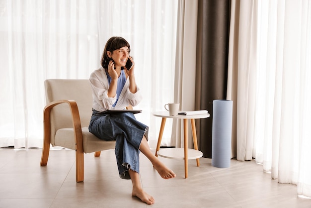 Volledige weergave van zakenvrouw zittend in een stoel in de kamer praten over de telefoon