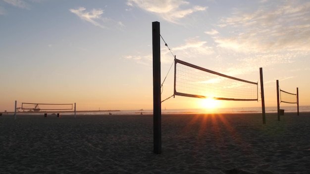 Volleyball net silhouette on beach court at sunset, California coast, USA. Sport field for volley ball game. Twilight sky background, sundown on Mission beach, San Diego, ocean shore near Los Angeles.