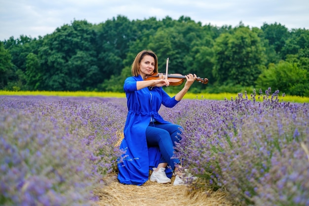 Vollieme volwassen vrouw violist die viool speelt en op het lavendelveld zit