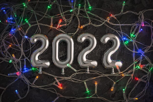 Объемные металлические серебряные цифры 2022 на черном фоне с гирляндами. Концепция приветствия на Новый год. Вид сверху.