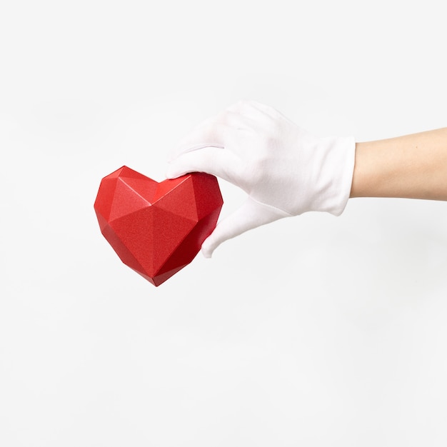 Volumetric paper heart  in hand with white textile glove on white background. Healthcare and medical concept.