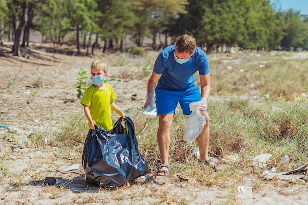 Volunteer blue face mask forest sand beach son helps father
hold black bag for pick up garbage problem spilled rubbish trash
planet pollution environmental protection natural children
education