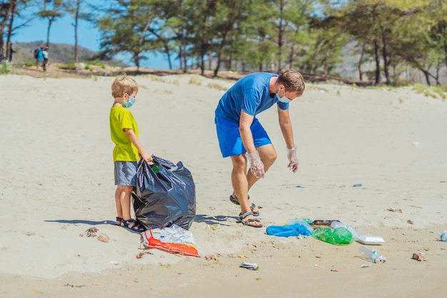 Volunteer blue face mask forest sand beach son helps father\
hold black bag for pick up garbage problem spilled rubbish trash\
planet pollution environmental protection natural children\
education