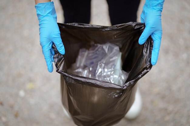 Foto mano della donna di beneficenza volontaria che tiene la borsa nera della spazzatura e la spazzatura della bottiglia di plastica per il riciclaggio per la pulizia al riutilizzo del concetto di volontariato del parco e aiuto volontario