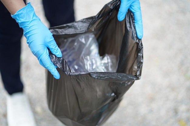 Volunteer charity woman hand holding garbage black bag and plastic bottle garbage for recycling for cleaning at park volunteering concept reuse and volunteer helping