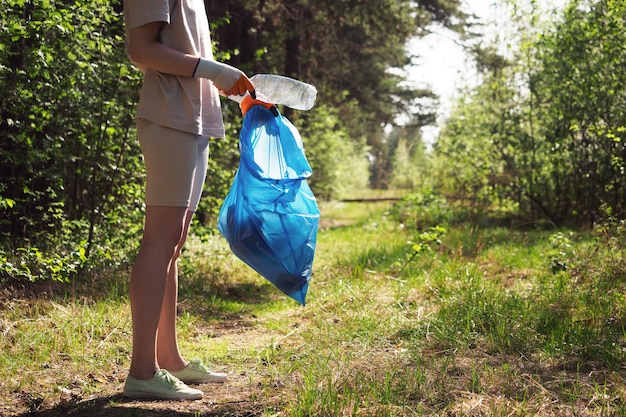 A volunteer and eco activist collects garbage in bags, in the forest, close-up. Recycling of plastic waste, environmental protection. Protecting the planet from debris. Ecology concept.