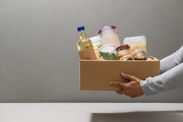 Volunteer in gloves holding food in a donation cardboard box with various food.