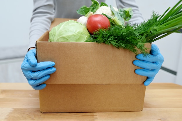 Volunteer in gloves holds food donation box vegetables to help the poor. Donat box with foodstuffs