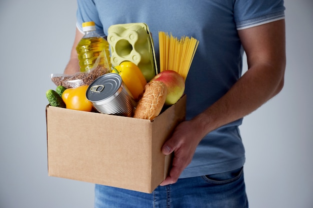 Volunteer holds cardboard box with donation food in hands in table