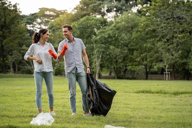 公園でゴミを集めるために歩いている手袋を着用したボランティア愛好家のカップル環境をきれいに保つために