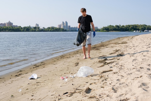 A volunteer man collects trash on the beach in a black bag Environmental problems