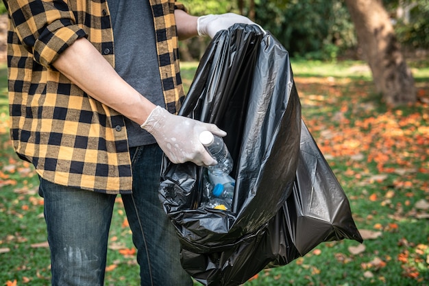 ゴミ収集までの環境活動中に公園を掃除するためにペットボトルをプラスチックの黒い袋に拾うために手袋をはめたボランティアの男