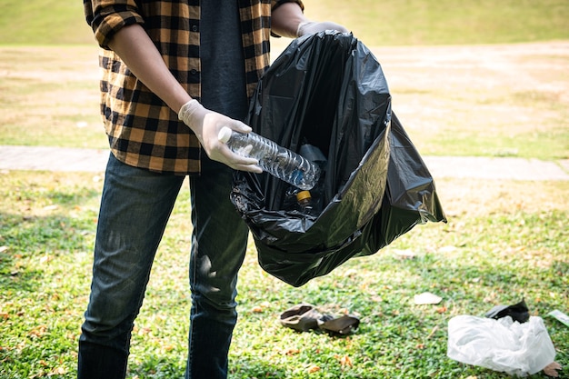 写真 ゴミ収集までの環境活動中に公園を掃除するためにペットボトルをプラスチックの黒い袋に拾うために手袋をはめたボランティアの男