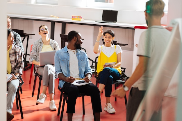 Foto volontario. studente abbastanza allegro alzando la mano e il seminario e gli altri studenti sorridendo e guardandola